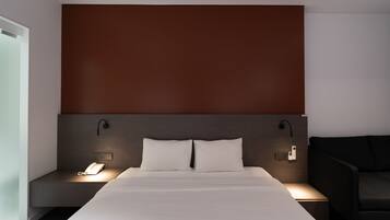Quarto de hotel moderno com uma cama grande, mesas de cabeceira, telefone e luminária fixada na parede.