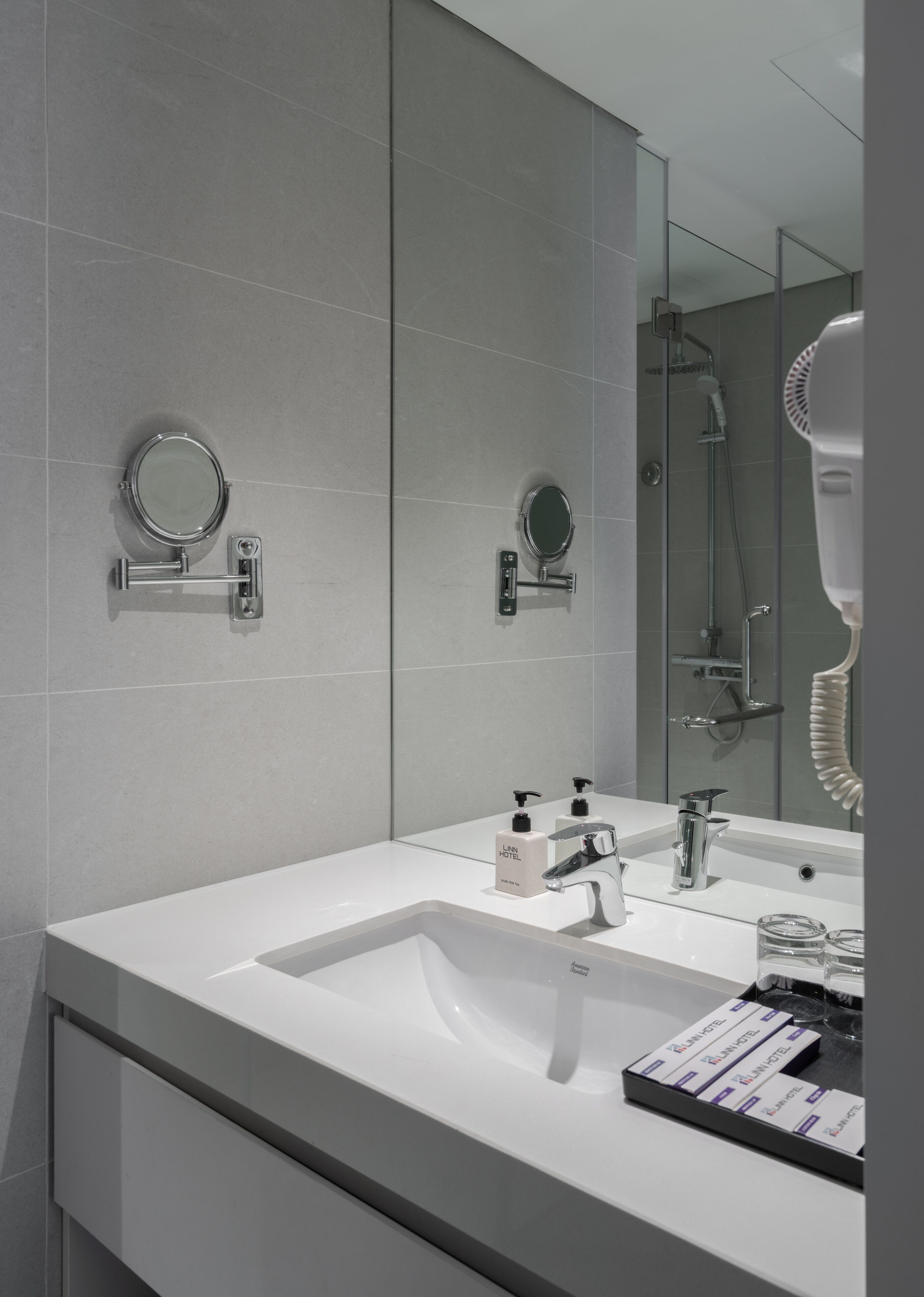 Un baño moderno con un espejo grande, dos lavamanos, ducha y secador de pelo.