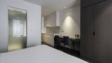 Habitació d'hotel moderna amb un llit, una taula de treball amb dues cadires, una cuineta i un armari.