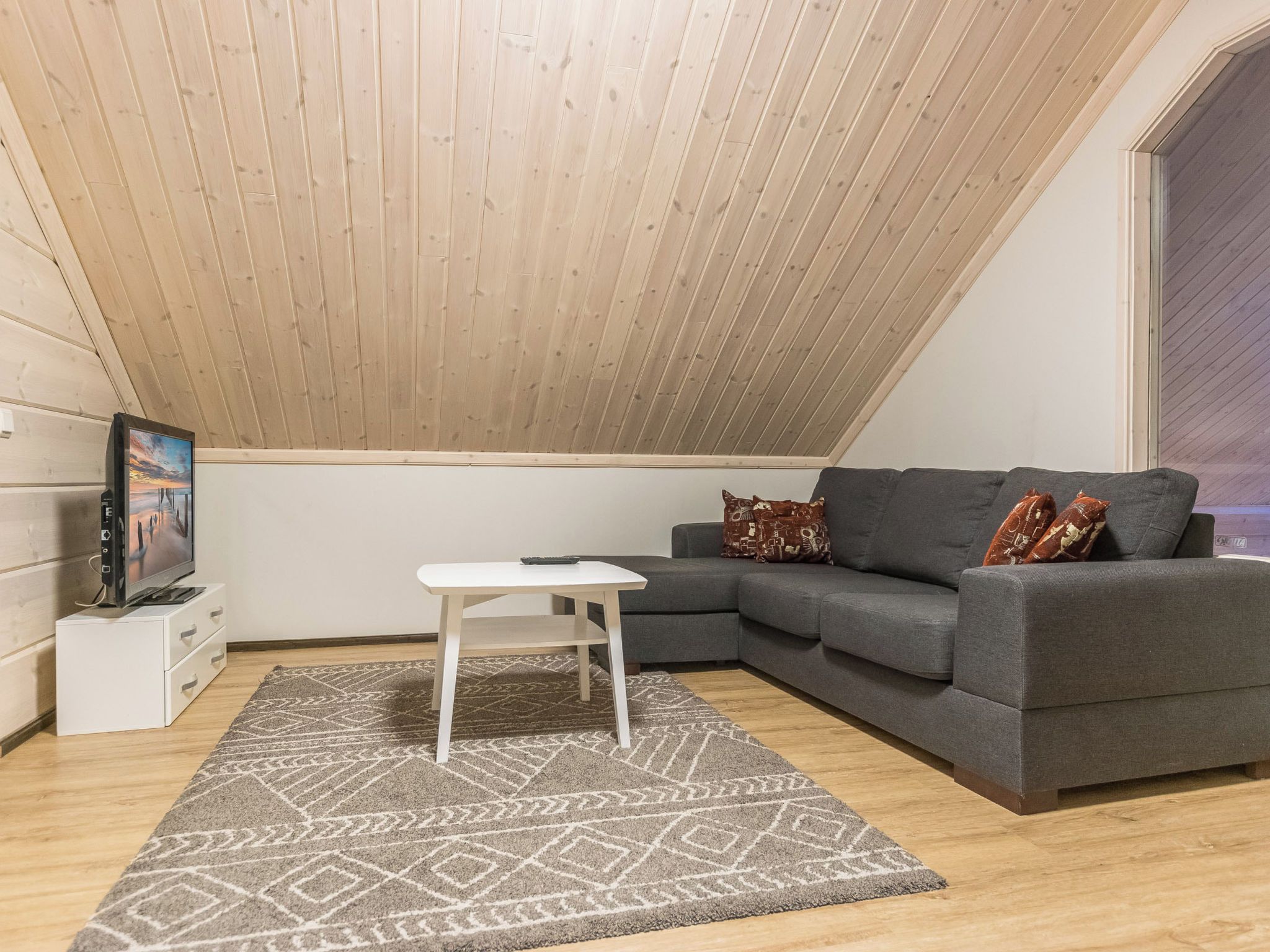 Ein modernes Schlafzimmer im Loft-Stil mit schrägverdeckter Decke, einem grauen Sofa, einem kleinen weißen Tisch und einem gemusterten Teppich.