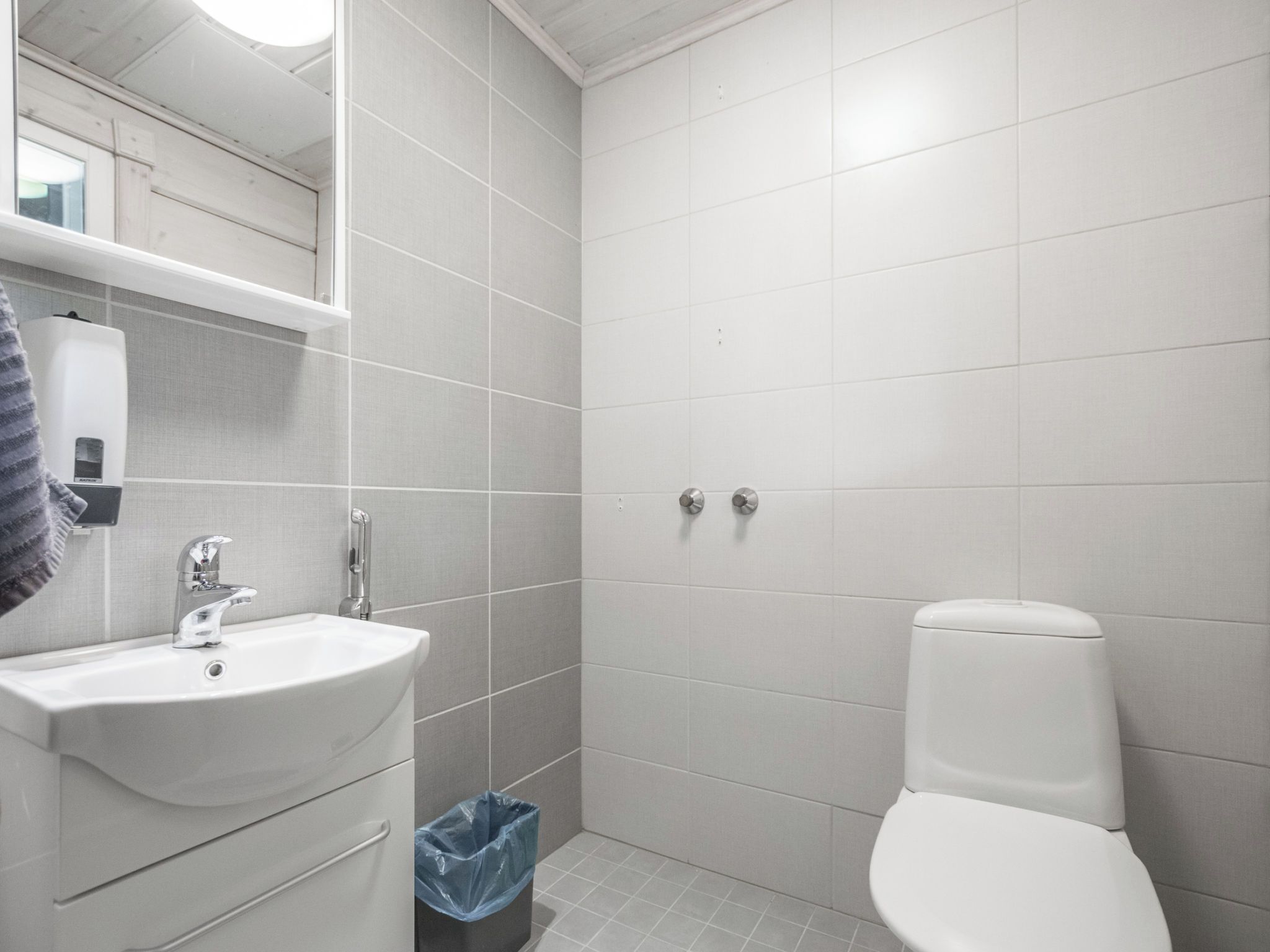 Une salle de bain avec un lavabo blanc, un miroir, des toilettes et une poubelle.