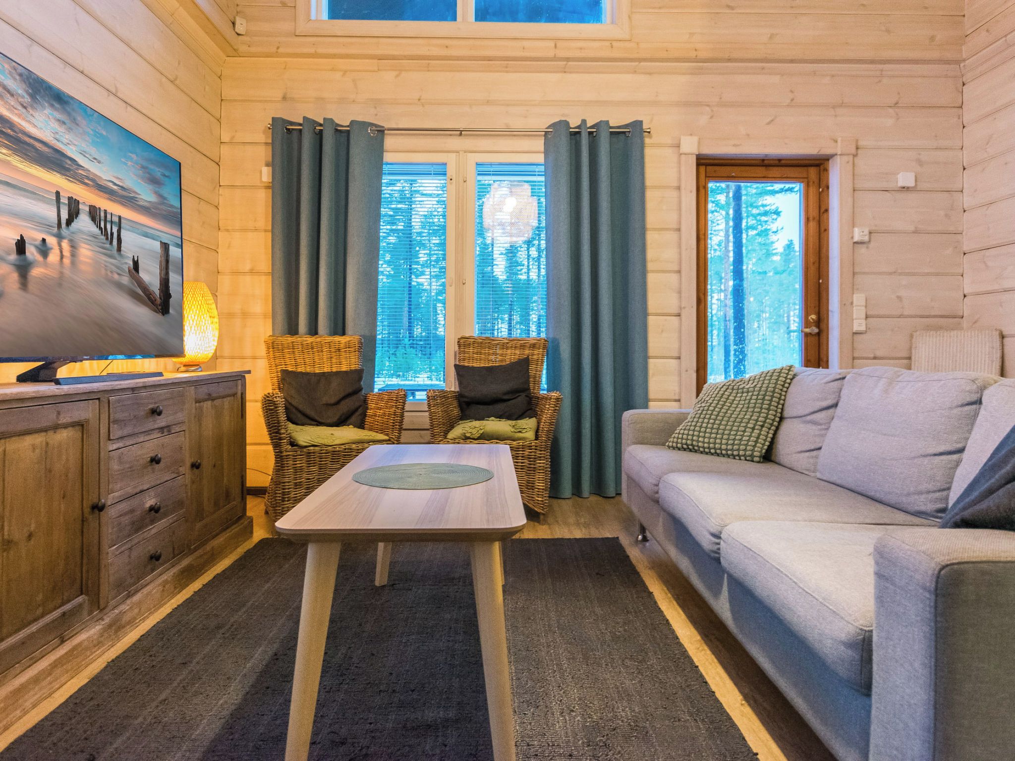 Een gezellige kamer met houten inrichting, een bank, een tafel en twee rieten stoelen.