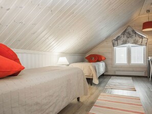 Ein gemütliches Schlafzimmer im Dachgeschoss mit geneigter Decke, zwei Betten mit roter und weißer Bettwäsche, einem Fenster mit Jalousien und einer Pendelleuchte.