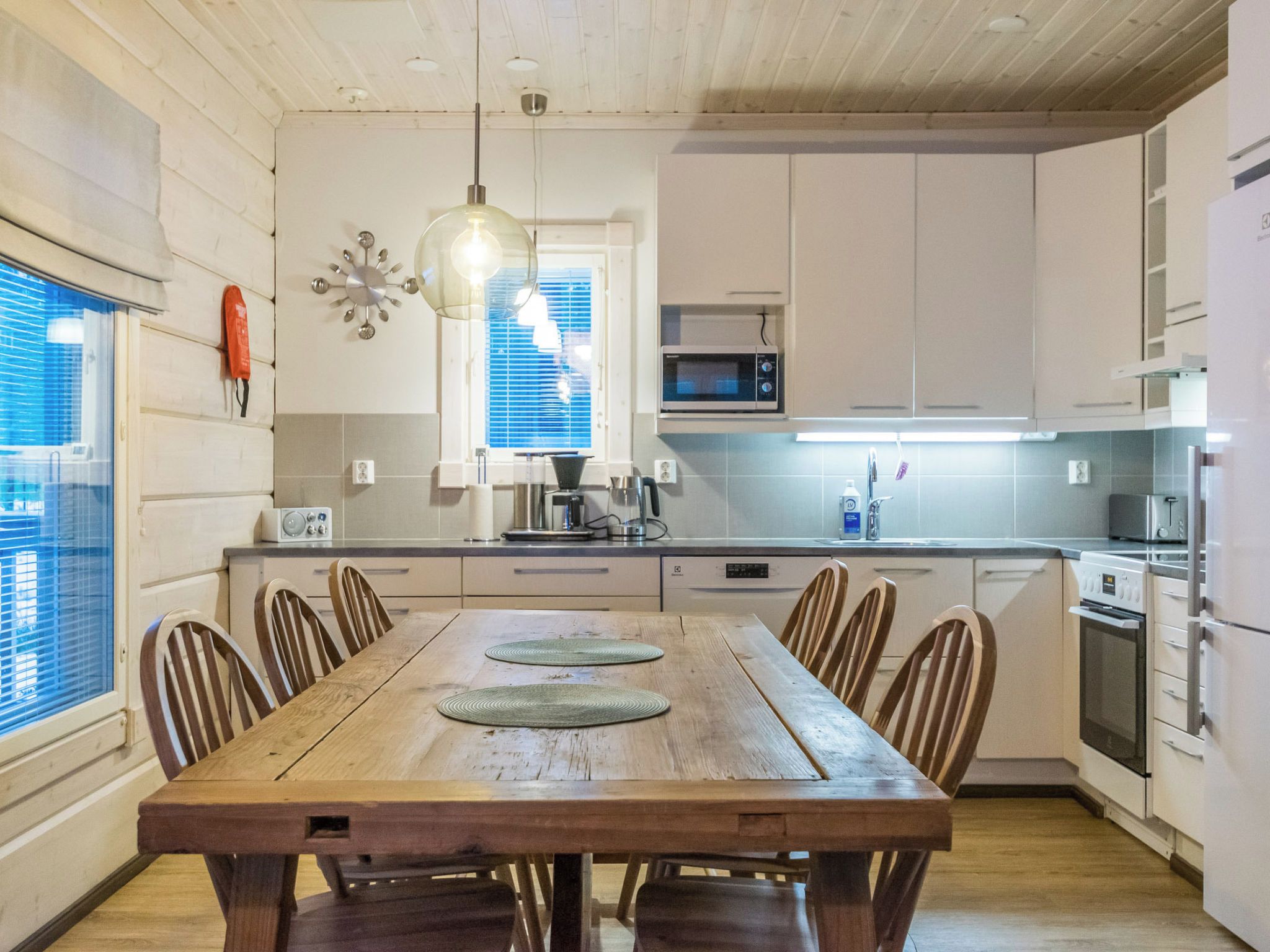 Una cocina moderna con armarios de madera, una mesa de comedor con sillas y una lámpara colgante.