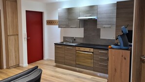 A modern kitchen with wooden cabinets, a red door, and a black countertop. - Meublés du 25 N°5 à Niederbronn-les-bains (Niederbronn-les-Bains)