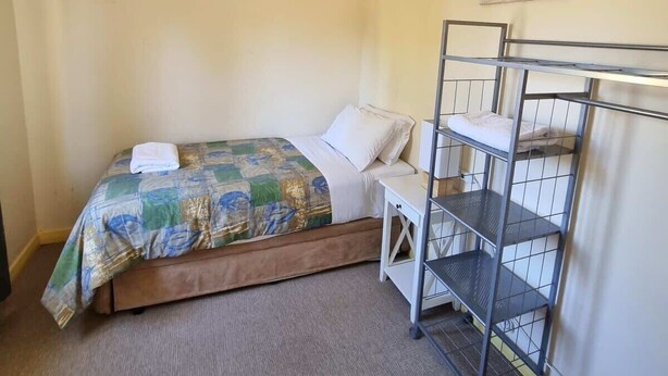 A single bed with a patterned blanket, a white pillow, a ceiling fan, an air conditioning unit, a metal bunk bed, and a wall-mounted shelf. - Kybunga by the Beach (part of Harriett's Cottage) (Largs North)