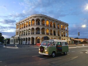 A green van with a Christmas wreath and lights parked in front of a building with multiple arches and balconies.