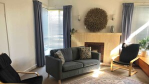 A living room with a sofa, two armchairs, a patterned rug, a fireplace, and a decorative wall piece. - Kybunga by the Beach (part of Harriett's Cottage) (Largs North)