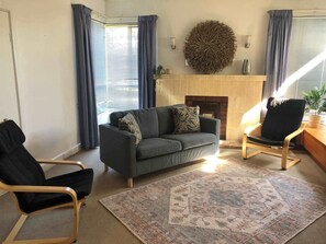 A living room with a sofa, two armchairs, a patterned rug, a fireplace, and a decorative wall piece.