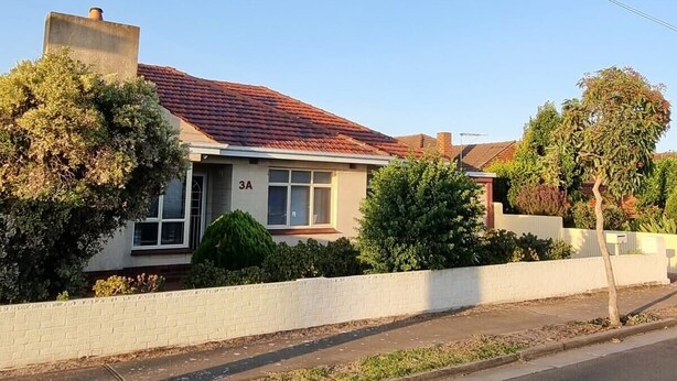 Une maison à deux étages, avec un toit recouvert de tuiles rouges, une cheminée en briques et une clôture blanche.