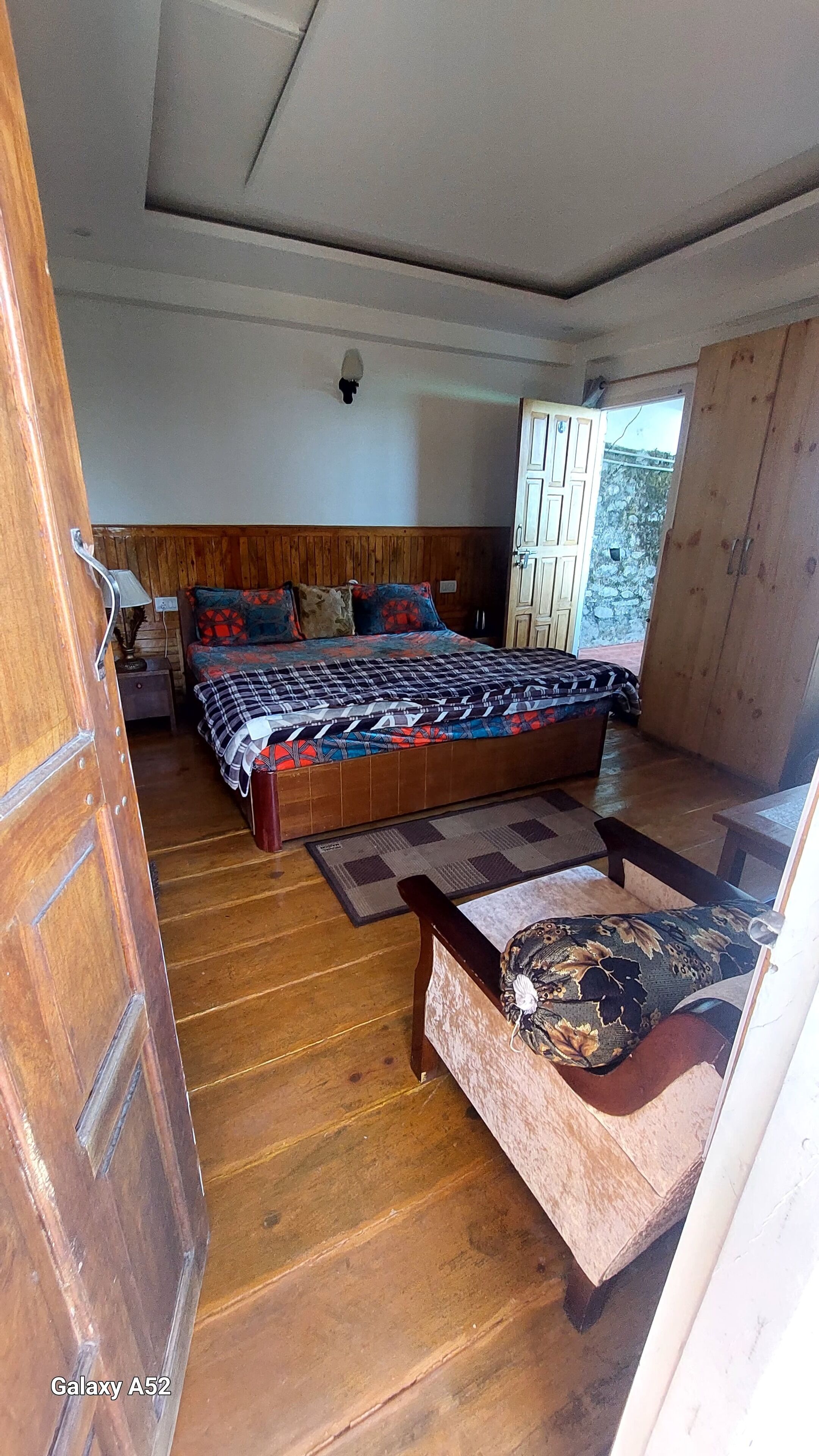A bedroom with a large bed, wooden flooring, a nightstand, and a wardrobe.