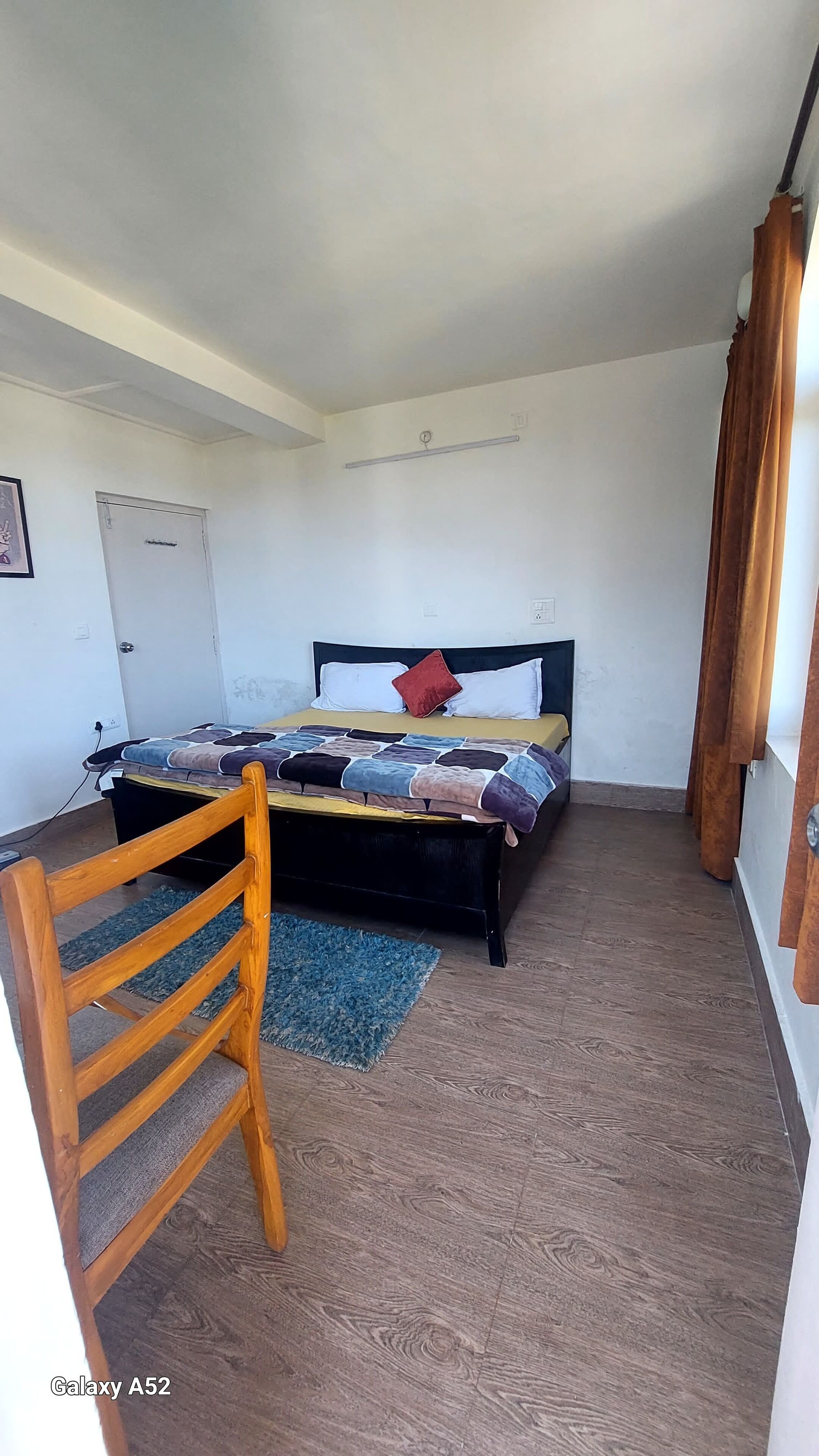 A bedroom with a bed, a wooden chair, a blue rug, and a door.