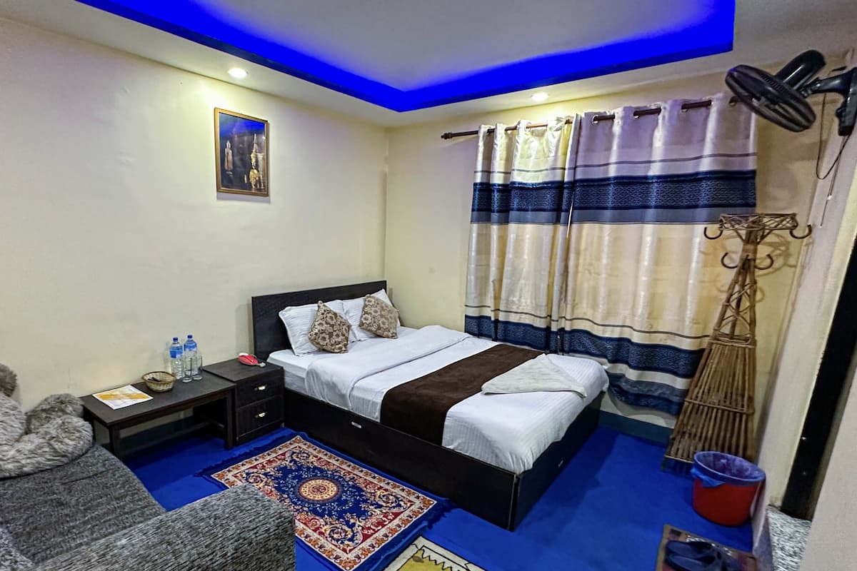 Un dormitorio con cama, mesitas de noche, sofá, alfombra decorativa, cortinas, ventilador de pared y televisor montado en la pared.