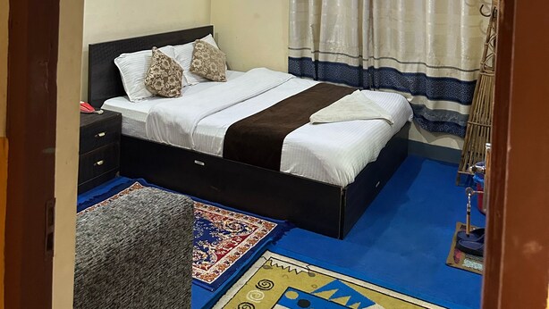 Un dormitorio con una cama, una mesita de noche, un ventilador de pared y una cortina.