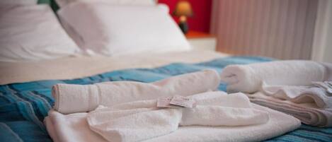 A neatly made bed with white pillows and folded towels on a blue striped bedspread.