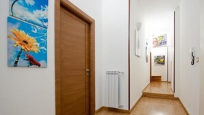 Un corridoio con pavimento in legno, un termosifone e una porta. Alle pareti sono esposti dei dipinti.