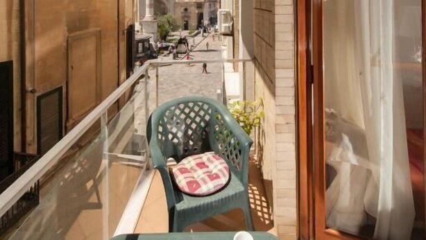 Un balcone con tavolo e sedie, vista sulla strada e una statua sullo sfondo.