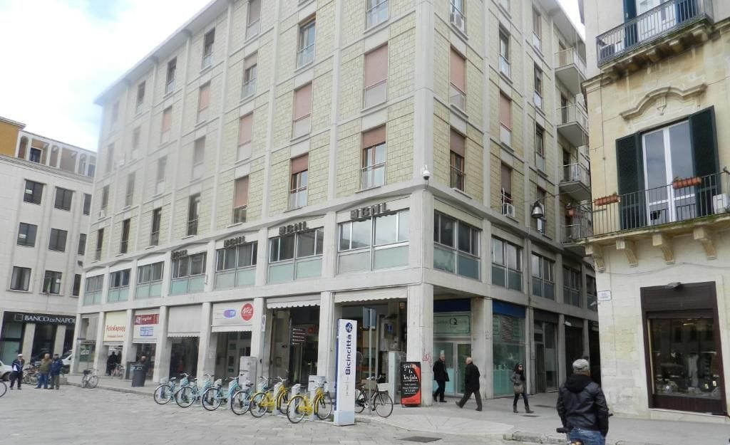 A multi-story building with a ground-level entrance, a sign for Bicincittà, and a row of bicycles parked outside.