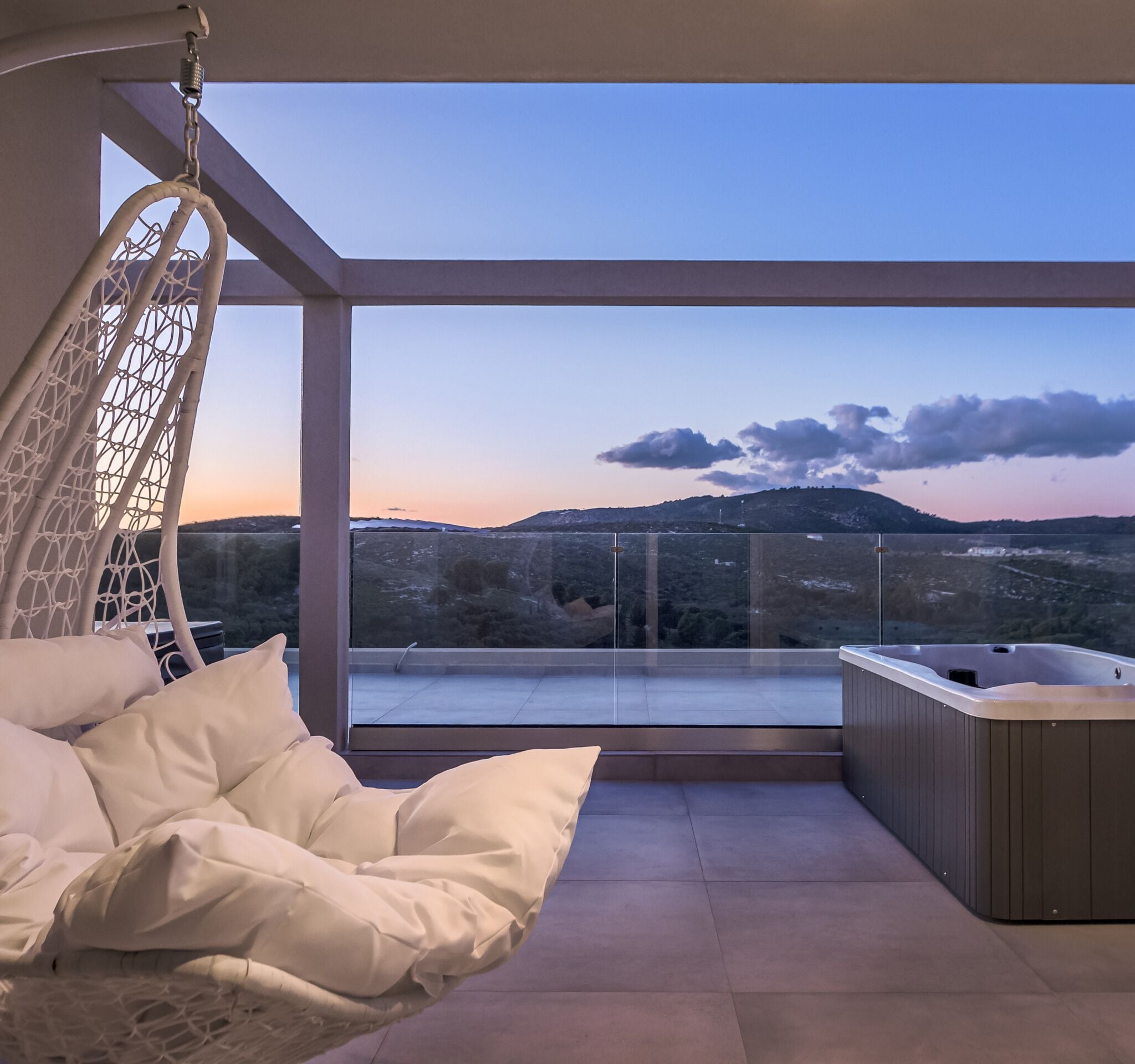 Un balcon avec un fauteuil suspendu, un jacuzzi et une vue sur les montagnes.