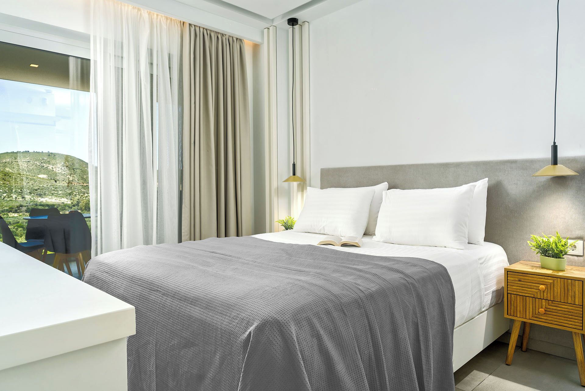 Et moderne hotelværelse med en stor seng, et natbord med en plante, og udsigt til det fri.