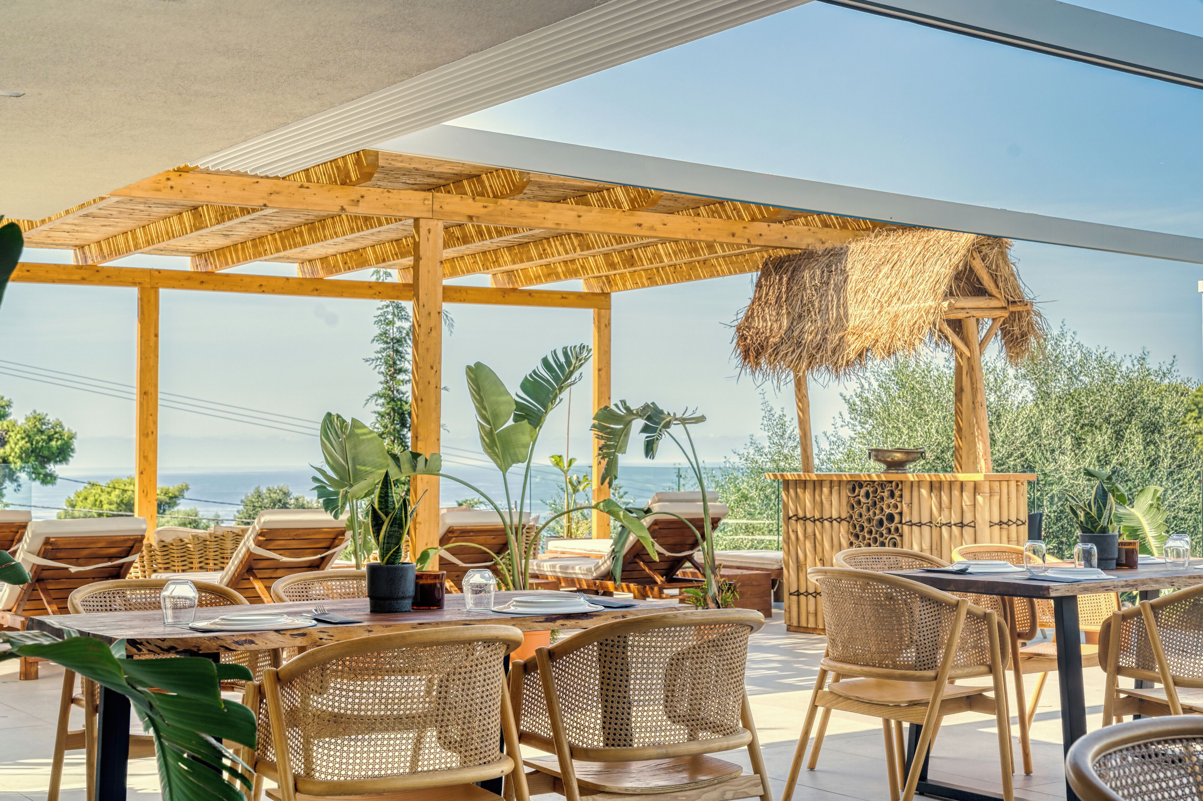 Een terras met rieten meubels, potplanten en uitzicht op zee.