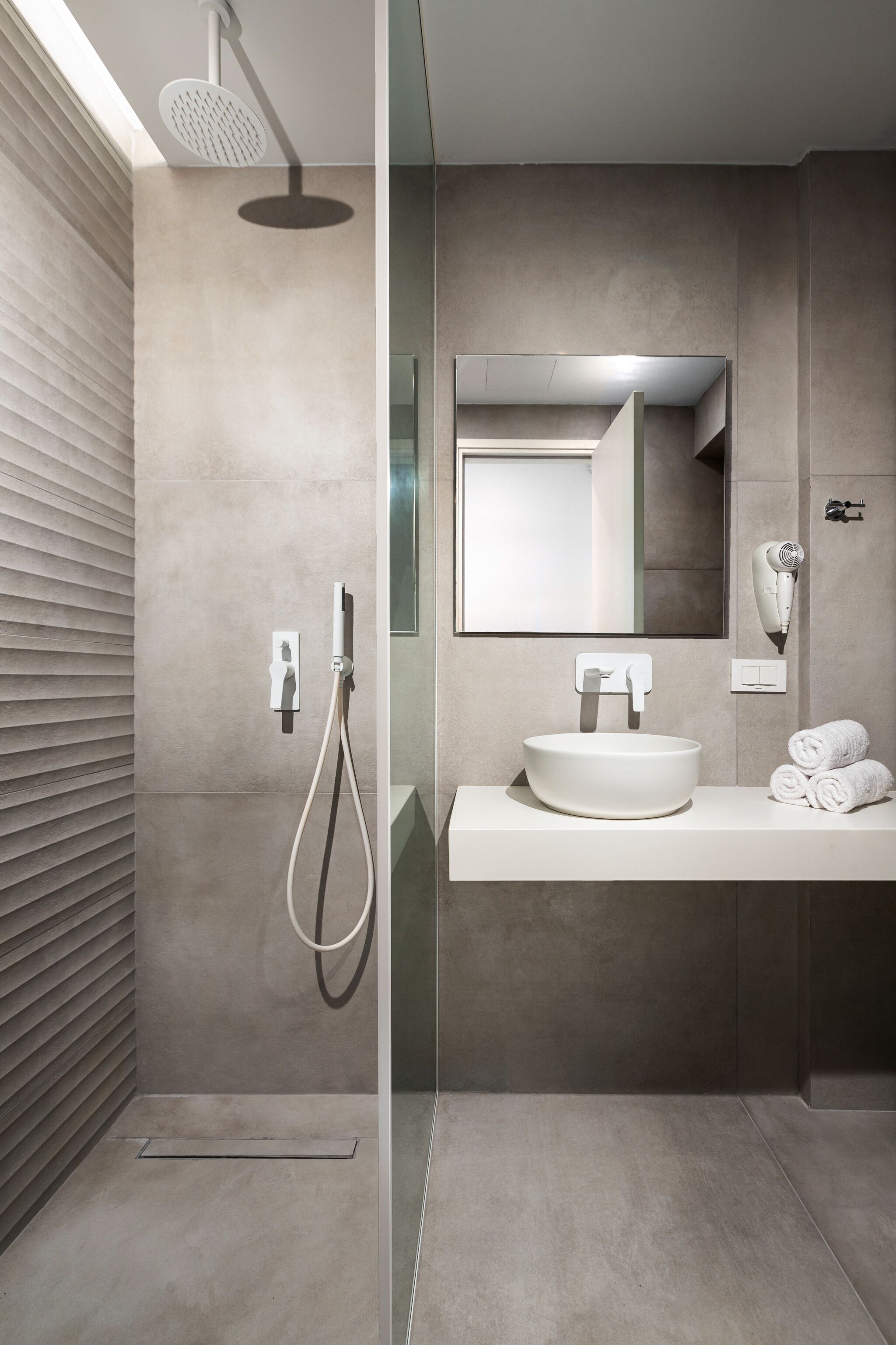A modern bathroom with a large mirror, a round sink, and a handheld showerhead.