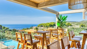 A terrace with wooden furniture and a view of the sea. - Myzith Luxury Suites (Zakynthos)