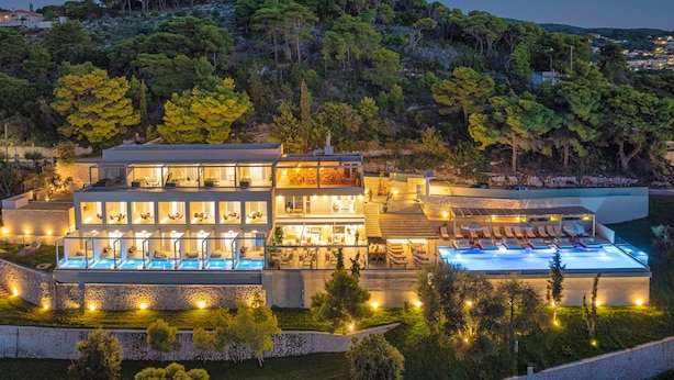 A modern multi-story building with a swimming pool, multiple balconies, and a lush surrounding landscape. - Myzith Luxury Suites (Zakynthos)