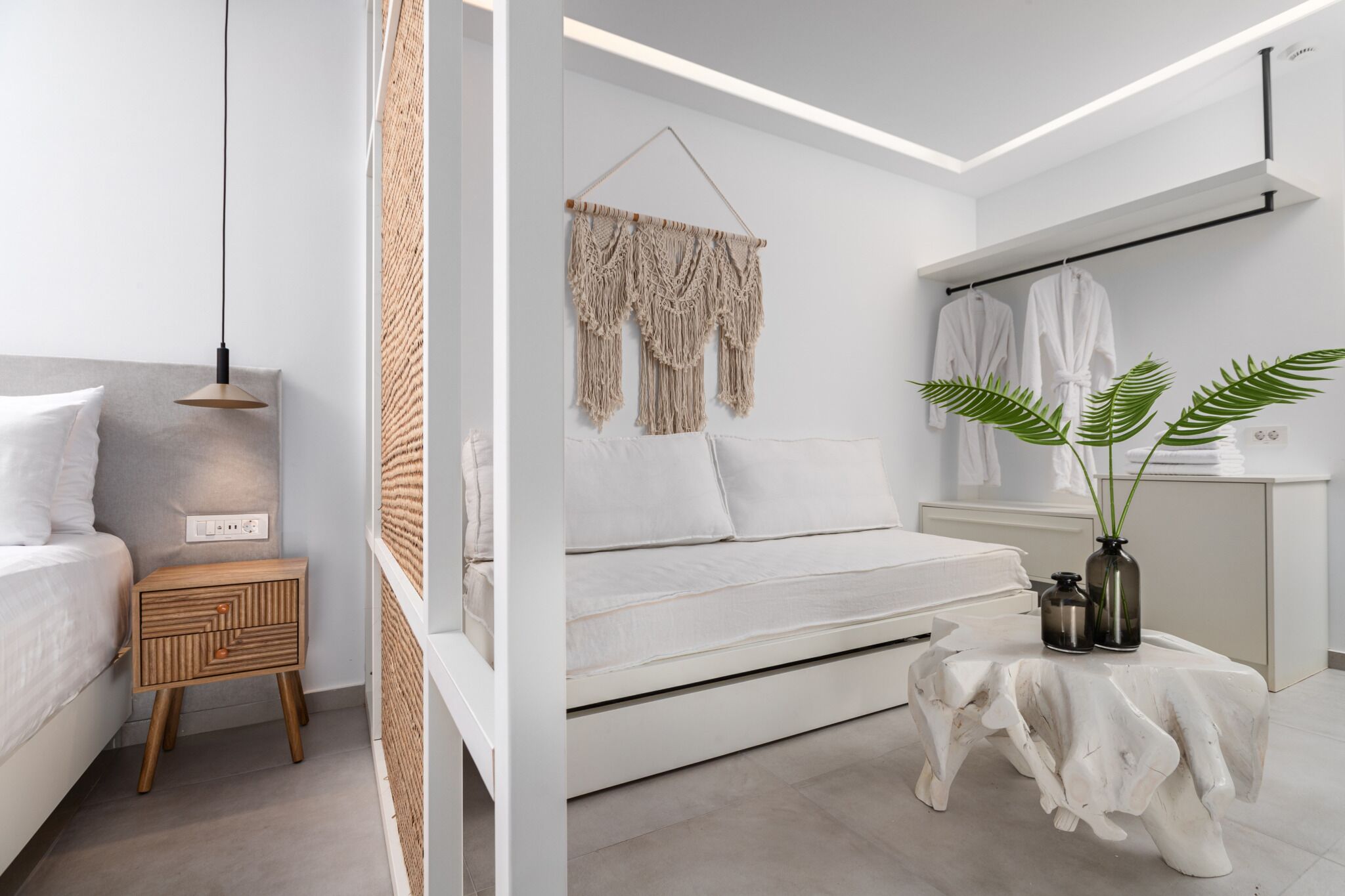 A modern bedroom with a bed, bedside table, hanging macrame wall decor, a plant, and a mirror with a towel rack.