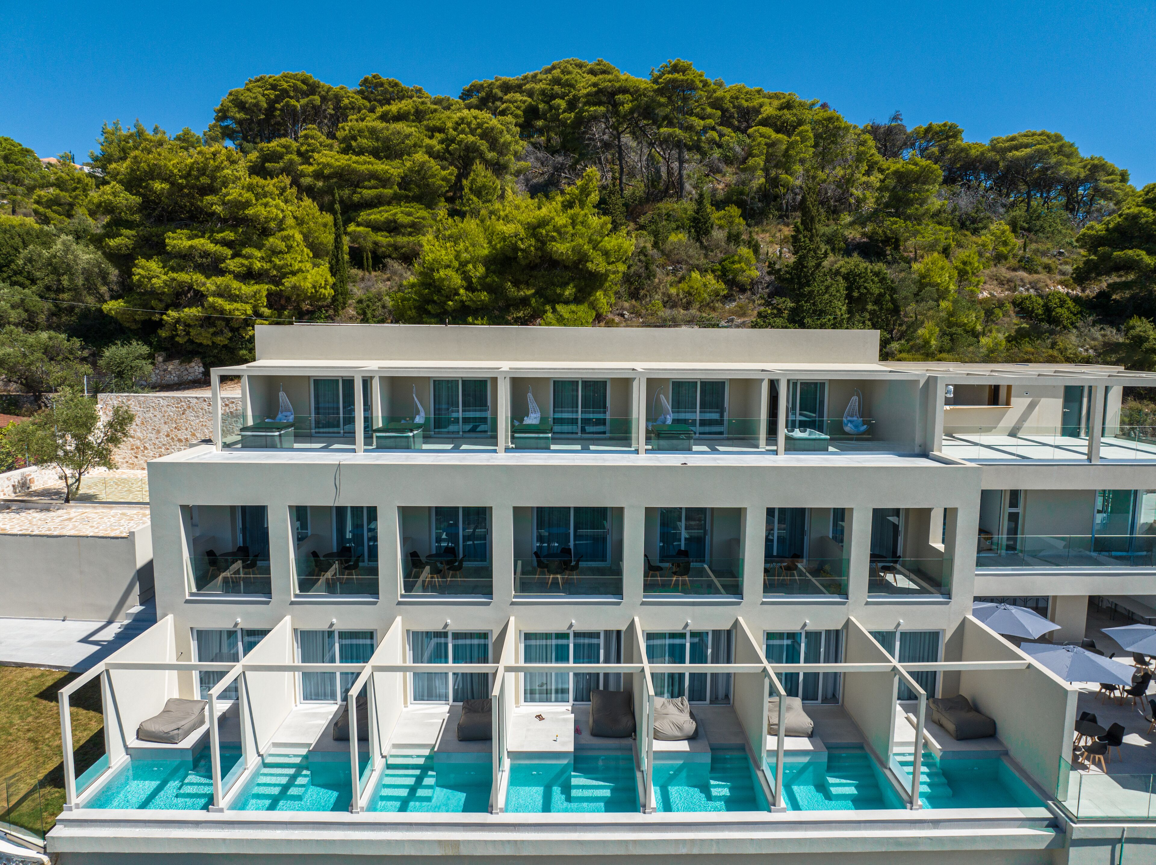 Ein modernes Hotel mit mehreren Balkonen, einem Swimmingpool und Blick auf einen bewaldeten Hügel.