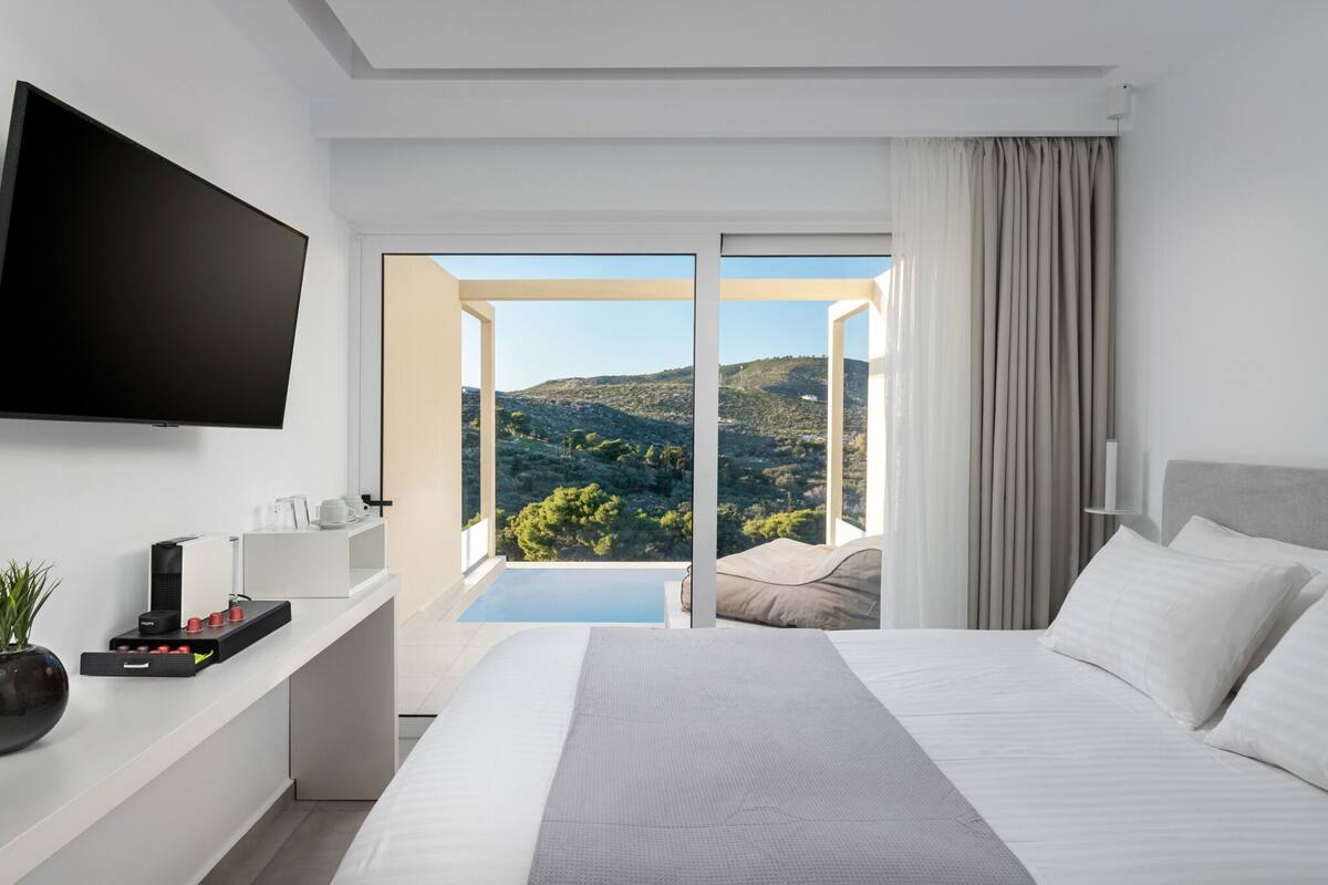 Habitación de hotel moderna con una cama grande, televisor de pantalla plana, cafetera y vistas a un paisaje montañoso a través de un ventanal corredera.