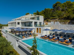 A modern hotel with a rooftop pool, outdoor seating, and a stone wall backdrop. - Myzith Luxury Suites  (Zakynthos)
