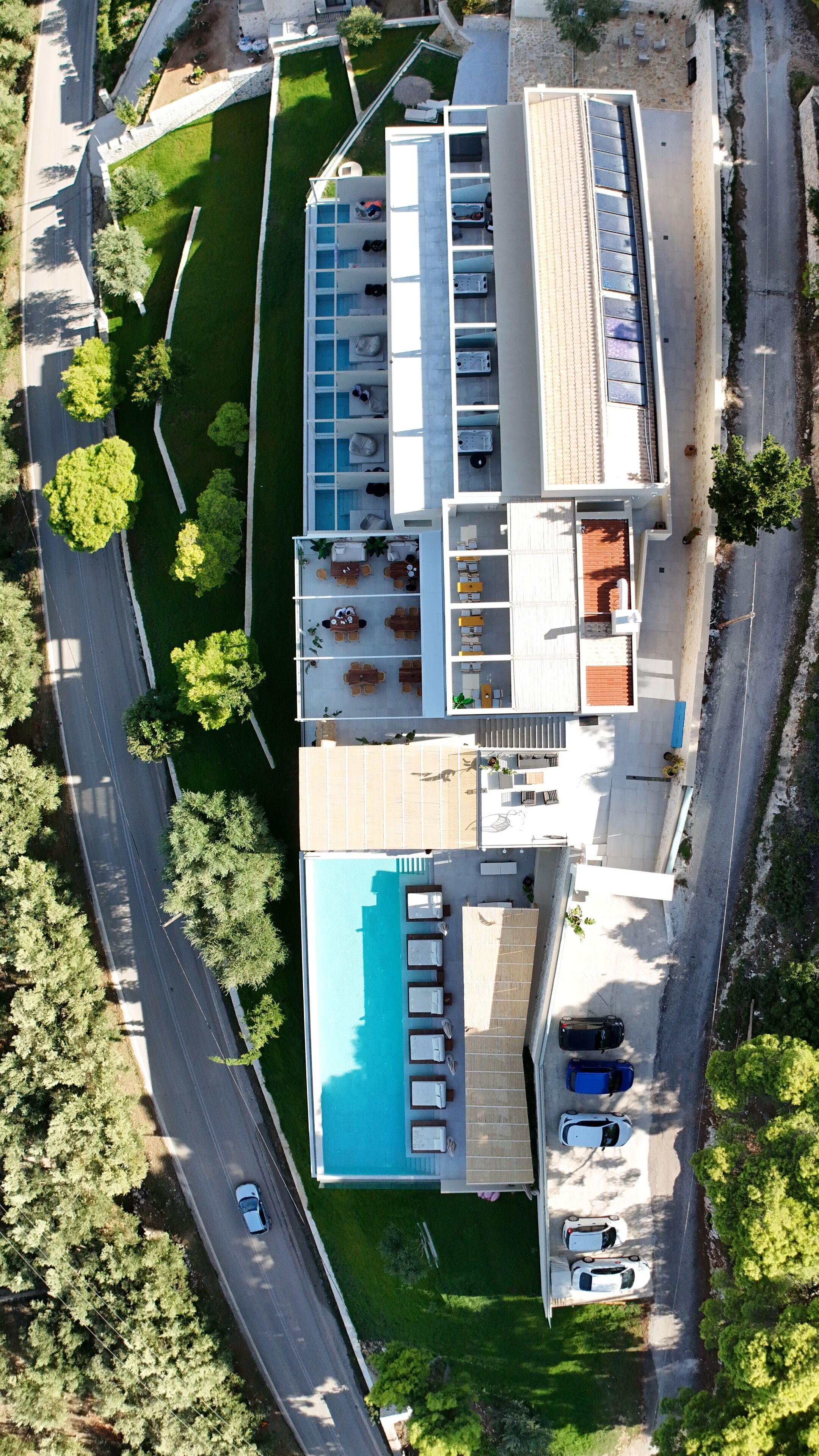 An aerial view of a modern hotel with a swimming pool, multiple balconies, and a parking area.