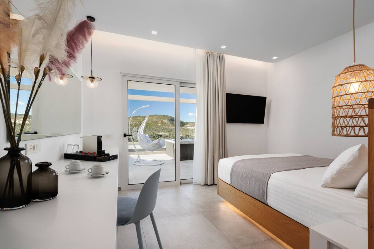 Una habitación de hotel moderna con cama, escritorio con silla, ventana grande y televisión en la pared.