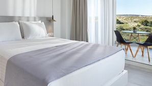 A modern hotel room with a large bed, a view of the countryside, and a small balcony with two chairs. - Myzith Luxury Suites (Zakynthos)