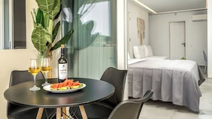 A modern hotel room with a dining area featuring a table with two glasses of wine and a plate of watermelon slices. - Myzith Luxury Suites (Zakynthos)