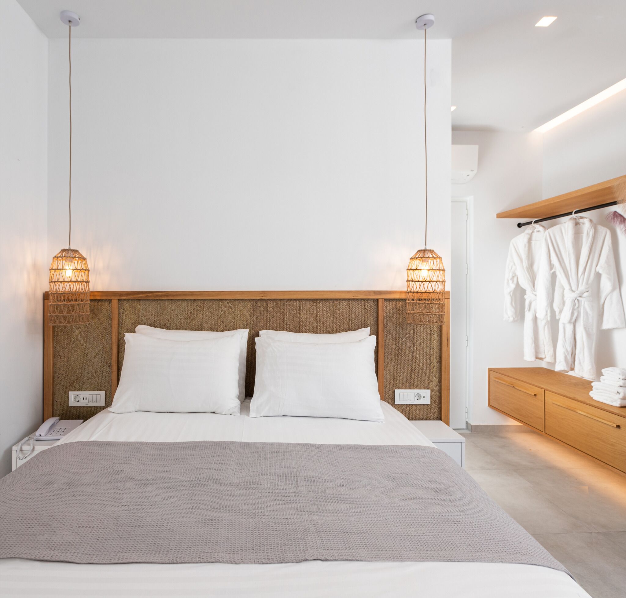 Una habitación de hotel moderna con una cama grande, dos lámparas de noche, un cabecero de madera, un teléfono en la mesita de noche y un aparador de madera con toallas.