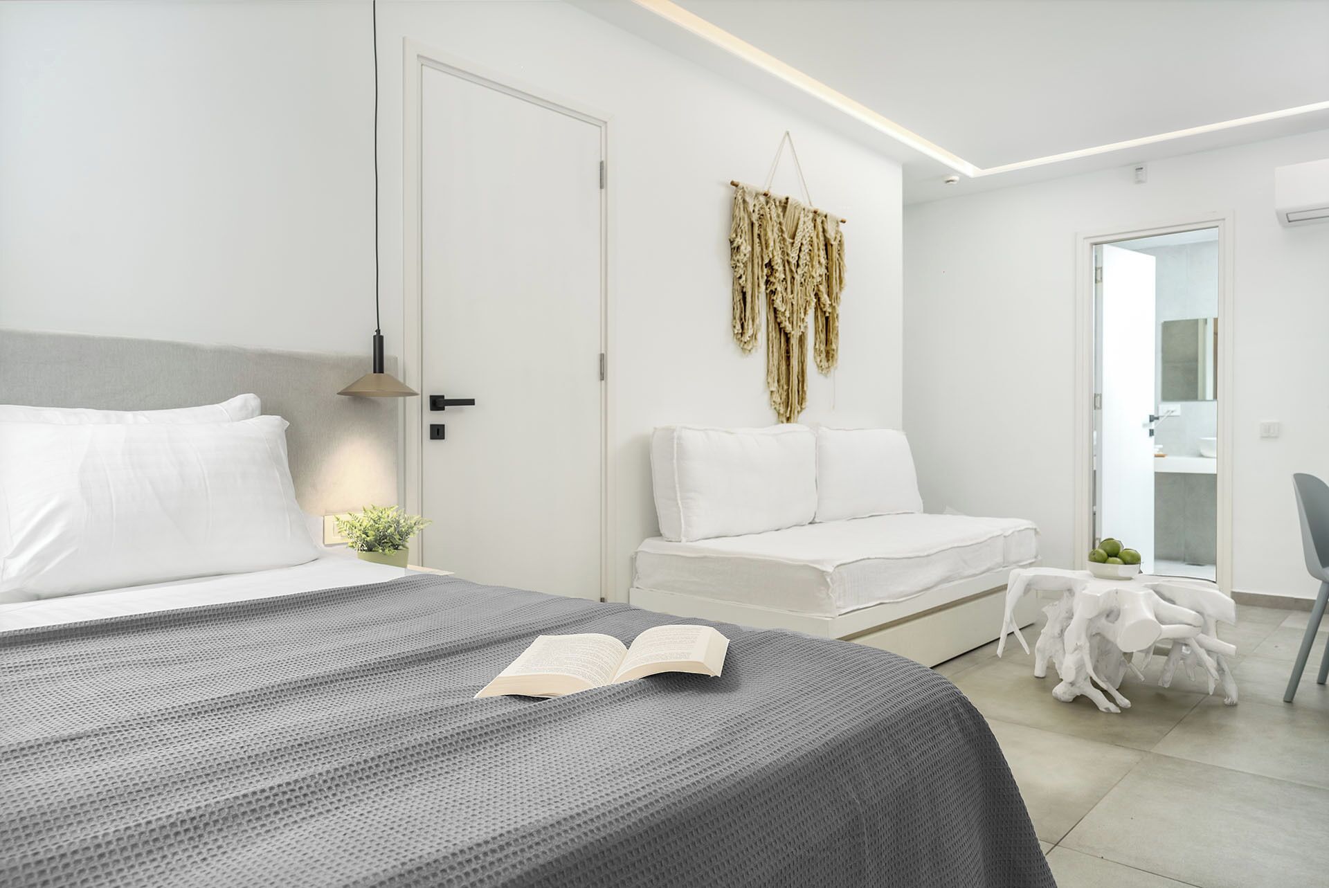 A modern bedroom with a bed, bedside table, and a reading area with a chair and small table.