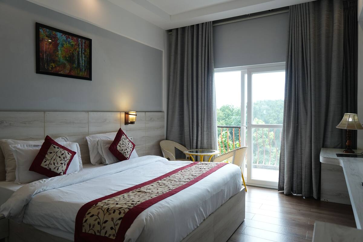 Een hotelkamer met een groot bed, een schilderij aan de muur, een balkon met een stoel en een tafel met een lamp.