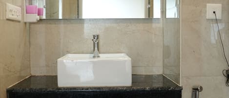A bathroom with a white sink, a mirror, a shower, and a trash can.