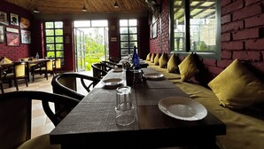 A restaurant with a long table, chairs, and a bench with yellow cushions. - AAR Resort and Spa (Dehradun)