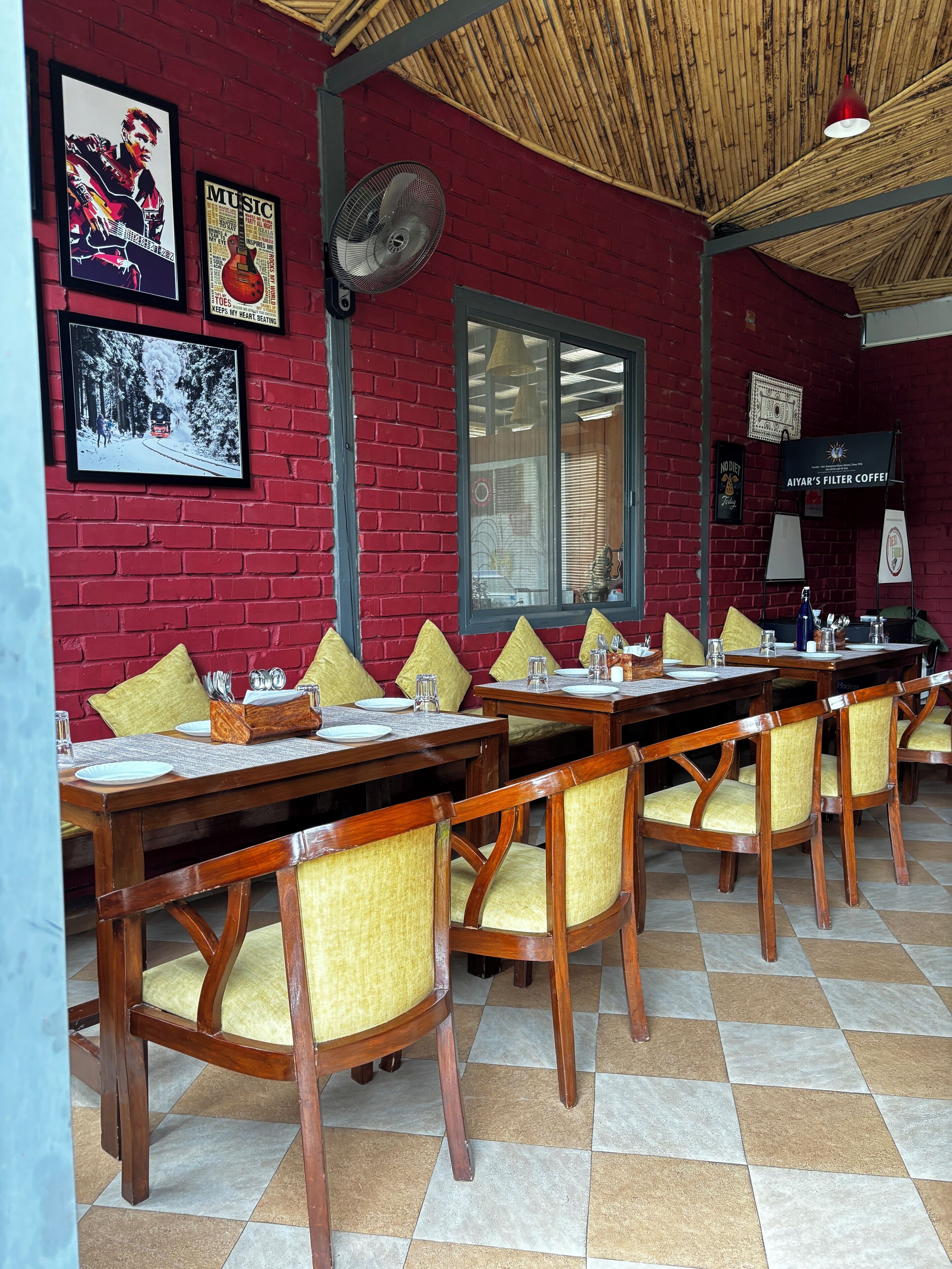 A restaurant with red brick walls, wooden tables, and yellow cushioned chairs.