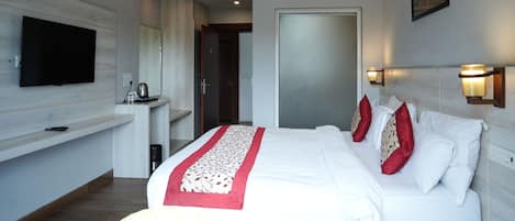 A modern hotel room with a large bed, a flat-screen TV, a small desk, and a painting on the wall.