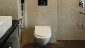 A modern bathroom with a marble wall, a toilet, a shower, and a sink. - AAR Resort and Spa (Dehradun)