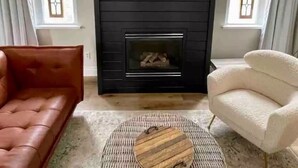 A living room with a black wall, a fireplace, a brown leather sofa, a white armchair, and a round wooden coffee table. - Delightful 2bdrm Church w/Incredible Water View!

 (Prince Edward)