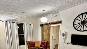 A living room with a white sofa, a brown armchair, a black storage unit, and a TV on a white wall. - Delightful 2bdrm Church w/Incredible Water View!

 (Prince Edward)