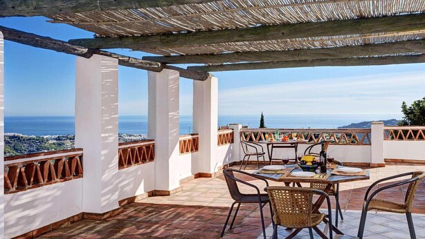 Un área de estar al aire libre techada, con mesa y sillas, con vistas panorámicas del mar.