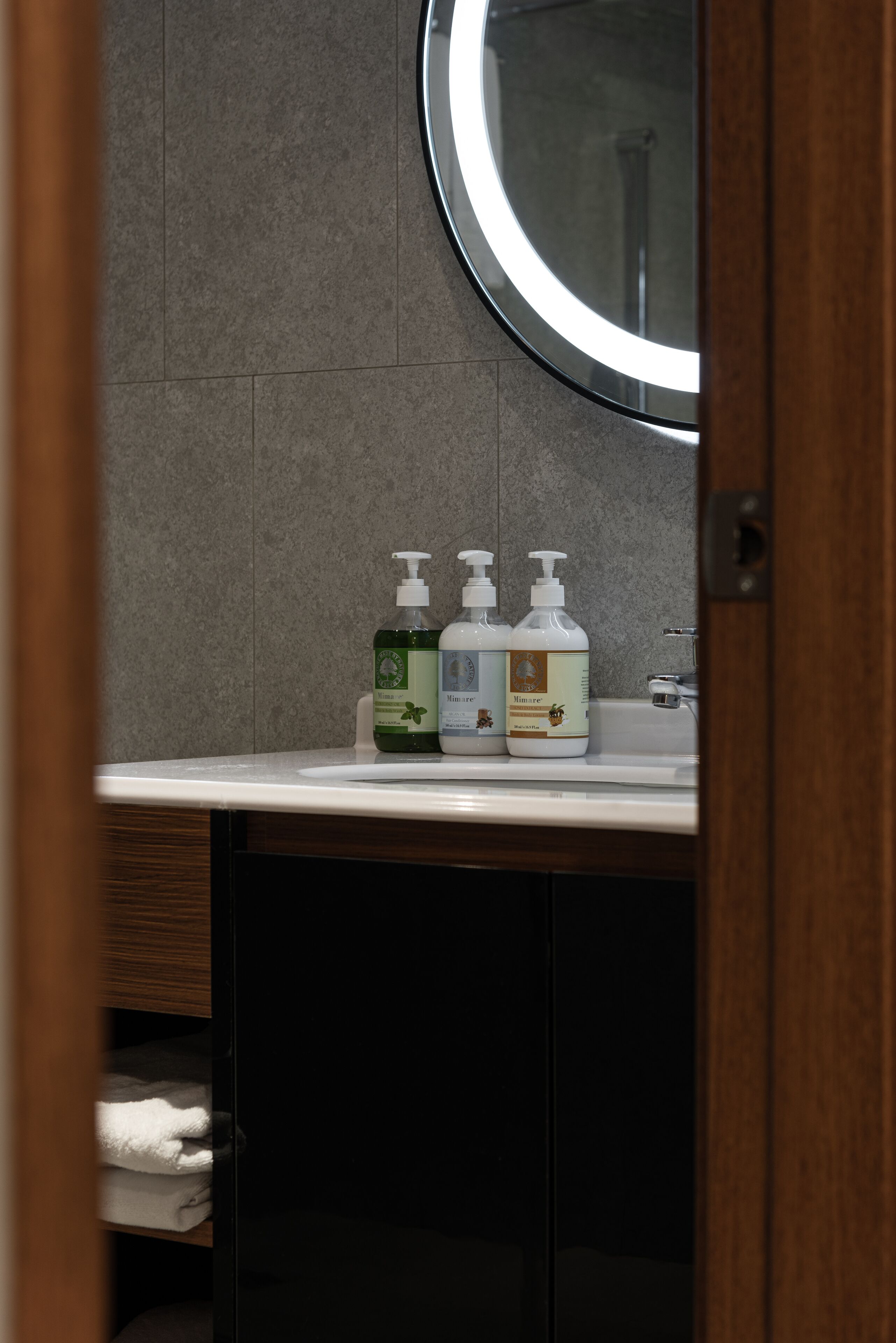 A bathroom with a white sink, two bottles of hand soap, and a round mirror.