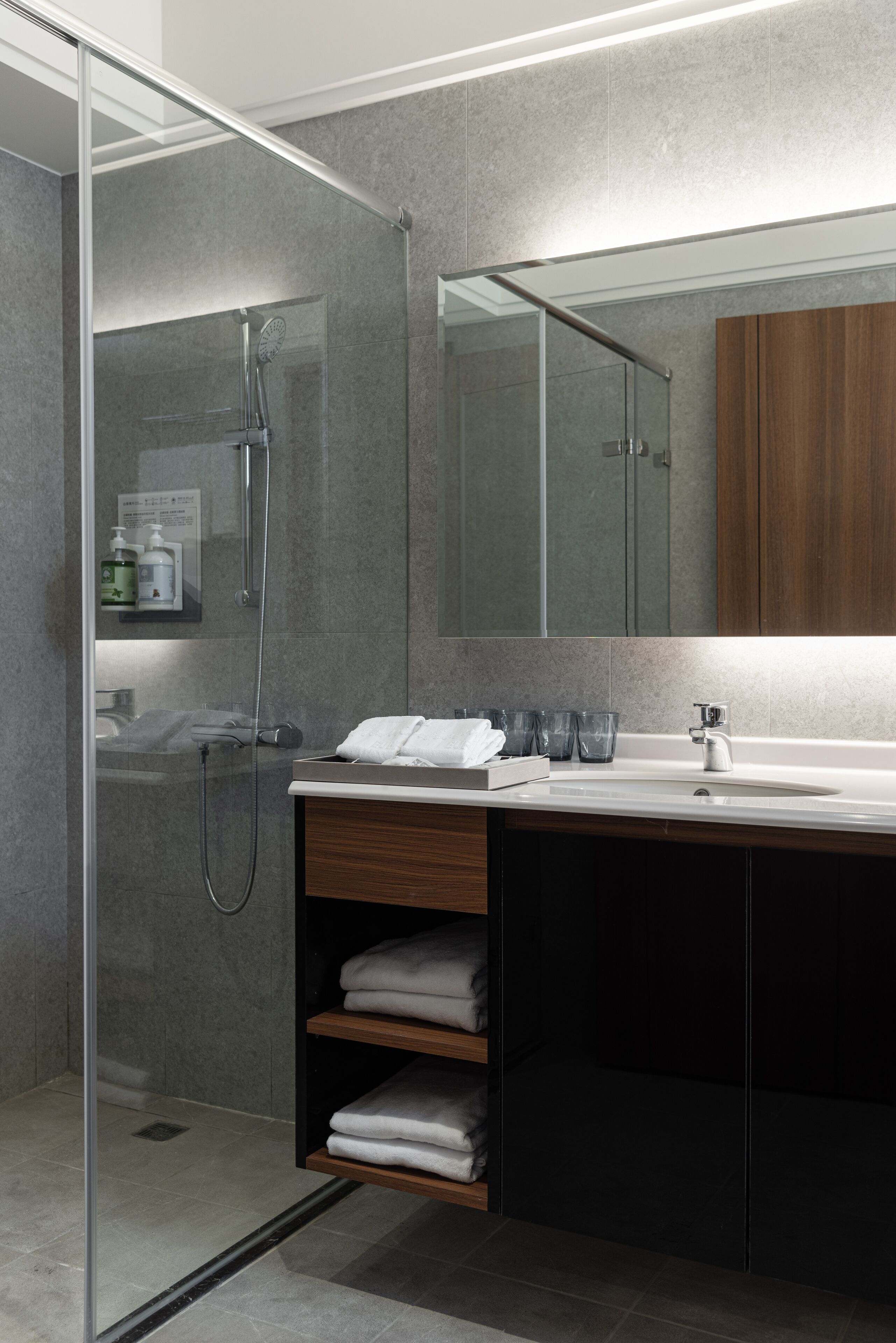 A modern bathroom with a glass-enclosed shower, a wooden vanity with a sink, and a large mirror above the vanity.