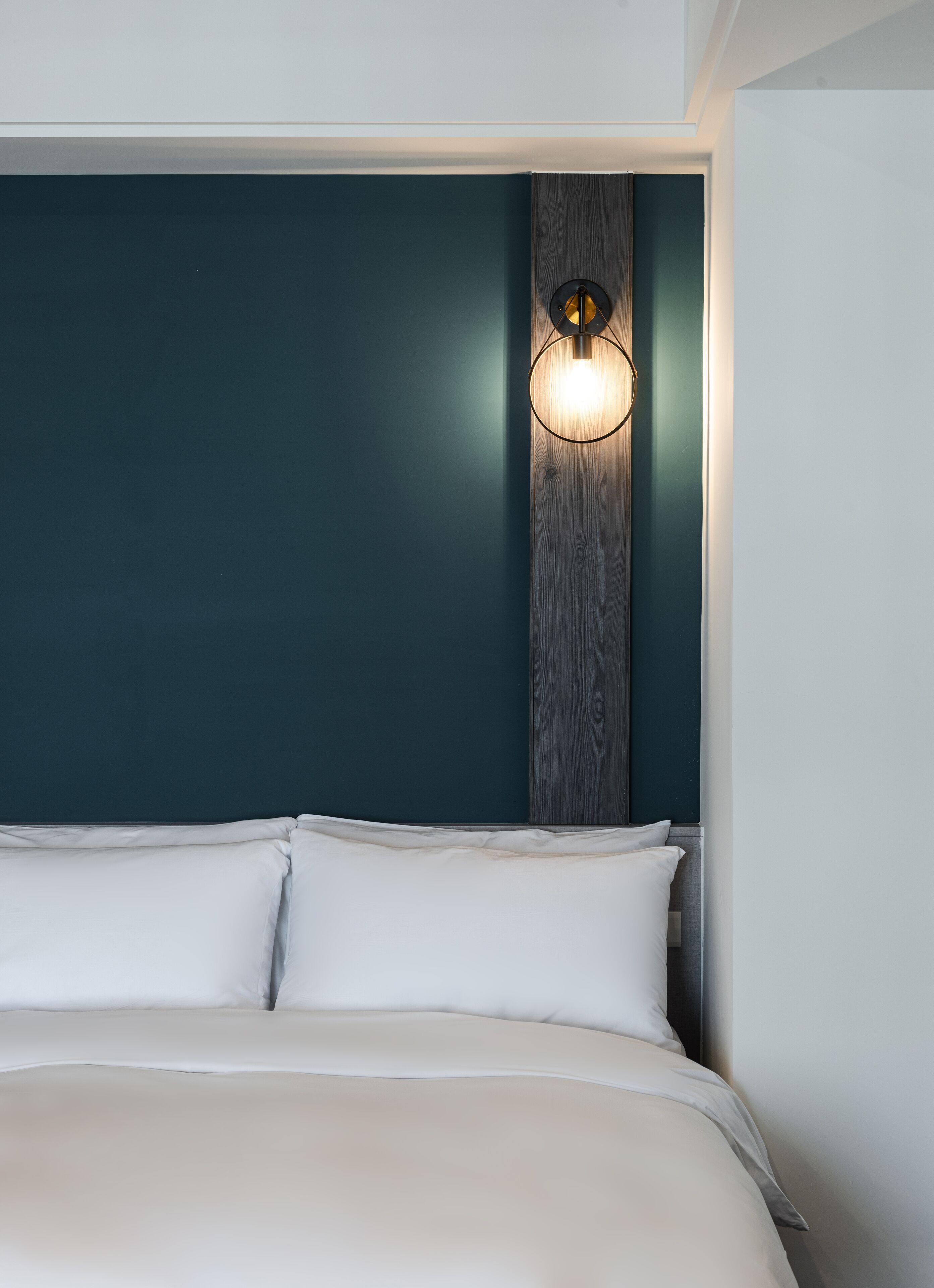 A bedroom with a bed, a wall-mounted light fixture, and a wooden panel on the wall.